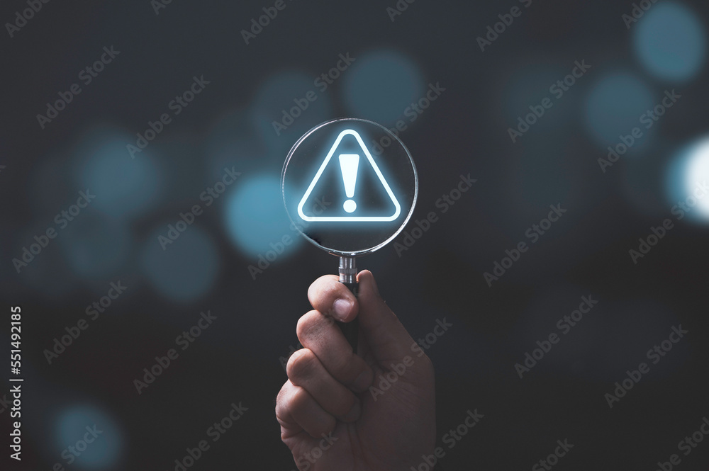 Wall mural hand holding magnifier glass with red triangle caution warning sign for notification error and maint