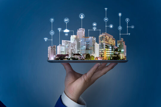Businessman hand holding tablet then land, trees and tall buildings on it, selling real estate online.