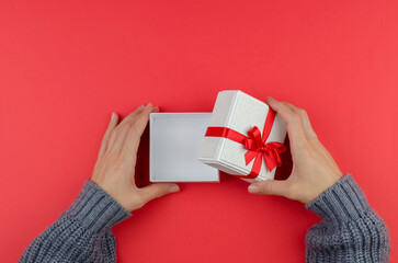 Open gift box in female hands on a red background. Woman opening a small gift box