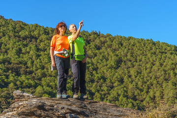 Two sympathetic female hikers pose at the top of the mountain, one woman pointing at the landscape.