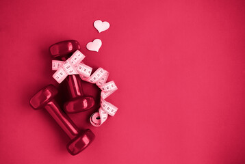 Two red dumbbells, white measuring tape, hearts on red background with copy space. Concept of...