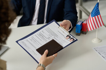 Close up of woman handing visa application form to worker in US Immigration office