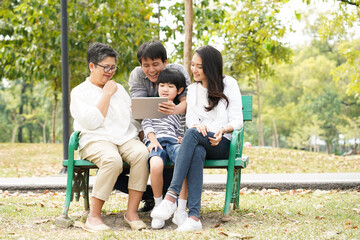 Happy Asian family have good moment and spend time together on holiday in the park by watching video on tablet with no generation gap good relationship life and insurance concept