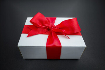 Gift box with a red ribbon on a black surface.
