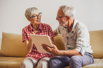 Senior couple sitting in living room and chatting with their family on digital tablet.