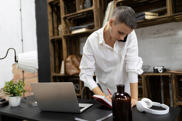 a woman with a short haircut works in the office talking on the phone making notes in a notebook