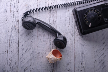 On a wooden surface with white shabby paint, a vintage black telephone, a beautiful sea shell lies...