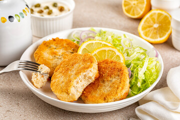 Eating Fish cakes or burger, or putties. Made from ground perch and tuna with herbs, breaded and fried, served with iceberg salad, lemon slices.