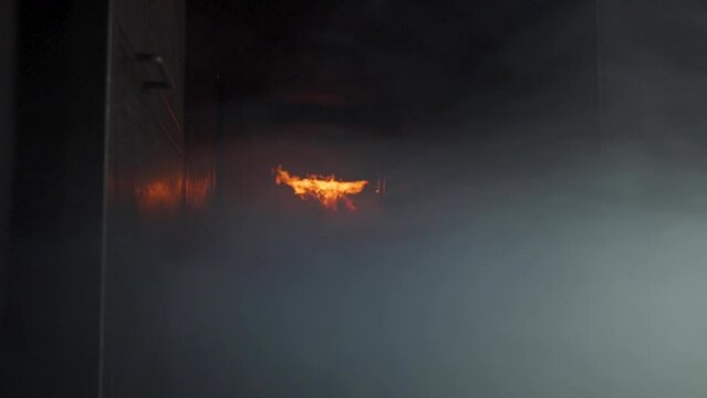 View inside burning building. Dark smokey room and orange flames ignite then roll down ceiling in flashover.