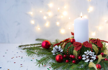 Festive winter Christmas wreath with a white candle, green branches and red balls on a white background. Christmas table decoration. Festive Advent time, copy space.