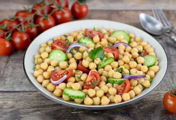 Chickpea salad with tomatoes, cucumbers, onions and herbs on a wooden background. Top view. Selective focus. 