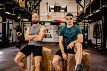 Two men sit on wooden boxes and look at the camera. Resting after a hard workout.