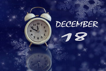 December 18 calendar: white alarm clock on a blue background with bokeh, reflection from objects, name of the month december, numbers 18