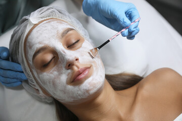 Cosmetologist applying mask on client's face in spa salon, top view