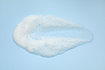 Smudge of white washing foam on light blue background, top view