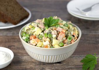 Russian traditional winter salad Olivier made of eggs, boiled vegetables, sausage, peas and mayonnaise with rye bread on a wooden background. Russian cuisine.