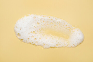 Spot of white washing foam on yellow background, top view