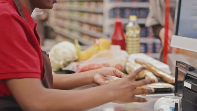 Female cashier in red uniform scanning food products while serving customers in supermarket