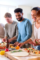 Group Of Friends At Home In Kitchen Adding Toppings To Homemade Pizzas For Party Together