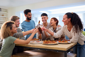 Friends Celebrating With Cheers At Home In Kitchen Eating Homemade Pizzas