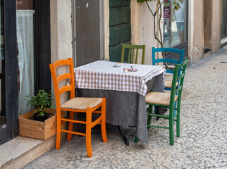 Fototapeta na wymiar Ein kleiner Tisch mit bunten Stühlen vor einem Strassencafe