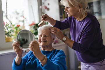 Woman combing hair of elderly mother 
 - obrazy, fototapety, plakaty