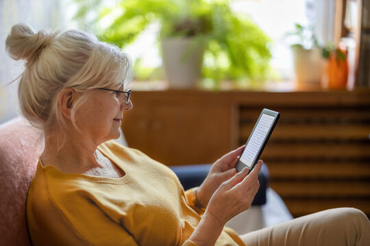 Senior woman using e-reader and reading an e-book at home
