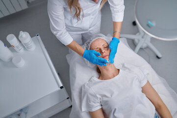 Woman professional doctor beautician applying mask on patient face for skin care