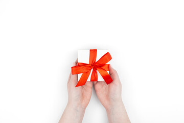 Gift box in a red ribbon in female hands on a white background, top view.