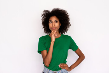 Portrait of thoughtful young woman looking away over white background. African American lady wearing green T-shirt and jeans posing with hand on chin. Thinking and planning concept