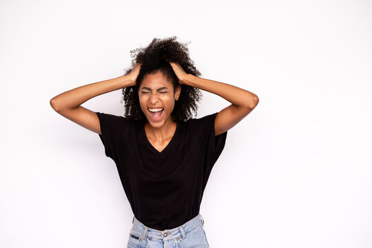 Portrait of young woman shouting in stress. African American lady wearing black T-shirt and jeans holding head in hands screaming in trouble. Problem or frustration concept