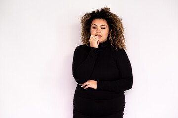 Worried young woman biting fingernail. Female African American model with curly hair and brown eyes in black turtleneck looking nervous hearing something unpleasant. Anxiety, trouble concept