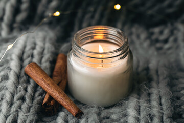 Close-up, candle and cinnamon sticks on the background of a gray knitted element.