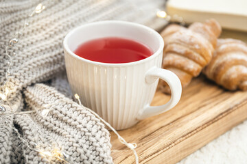 Obraz na płótnie Canvas A cup of red tea, a croissant and a knitted element on a wooden tray.