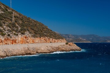 Turkey. Fethiye. View of Turkish Mediterranean coast. Automobile road along mountains on the coast. Emerald water washes shore. Blurred background. Selective focus. Wild Mediterranean beach.