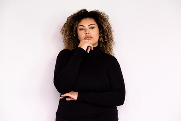 Thoughtful young woman holding hand on her chin. Female African American model with curly hair and brown eyes in black turtleneck touching chin with her hand. Advertisement, thought concept