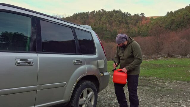 A man pouring gasoline into fuel tank from a plastic red gas can. Offroad fuel reserve.