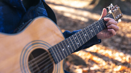 Close-up, a man plays an acoustic guitar in the autumn forest.