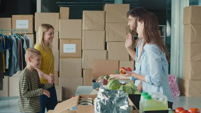 Friendly Volunteer Giving Donation Box With Food to Woman and Her Son at Distribution or Refugee Assistance Center. The Concept of Social Aid. Internally Displaced Persons