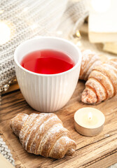 A cup of red tea, a candle, a croissant and a knitted element on a tray in bed.