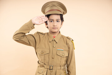 Indian boy kid wearing police custom dress salute isolated on beige studio background. Dream,