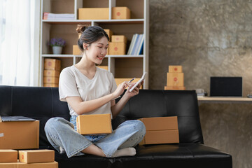 delivery concept SME, freelance Asian woman smiling using laptop computer with joyful success of boxed items, online marketing, selling at home.