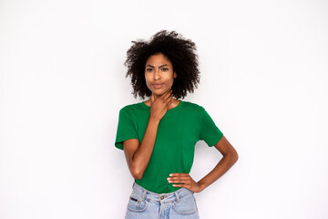 Portrait of unwell young woman touching aching throat over white background. African American lady wearing green T-shirt and jeans suffering from cold. Pulmonary diseases concept