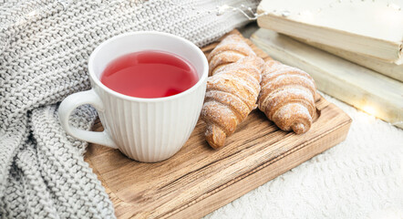 A cup of red tea, a croissant and a knitted element on a wooden tray.