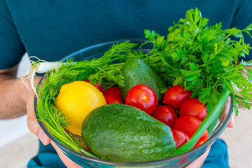 A man holds a large bowl with fresh vegetables and herbs.