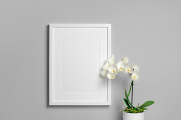 Blank portrait frame mockup on grey wall with white orchid flower
