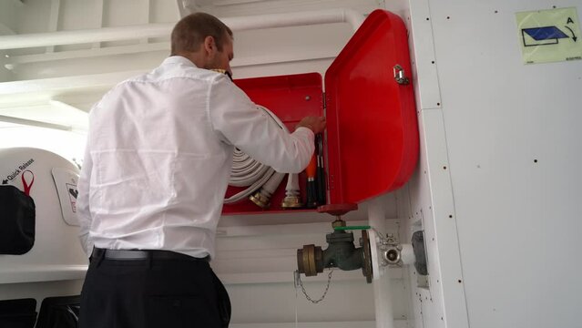 Ships captain inspecting firehose - Firefighting equipment onboard passenger ship is controlled - Static low angle looking up at box and male captain