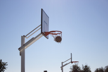 Low angle shot of basketball getting right into hoop outside on sunny day. Clean ball throw into basket with white backboard against blue cloudless sky. Achievement, sports concept