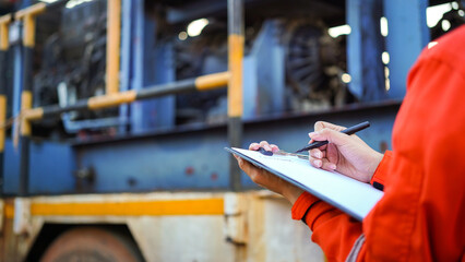 An engineer is writing on paper the list the maintenance detail with a heavy pumping machine as...