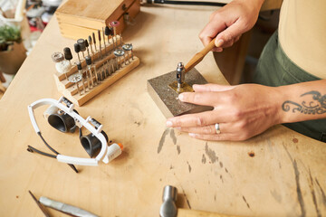 Top view closeup of tattooed female artist creating handmade jewelry ion wooden workstation